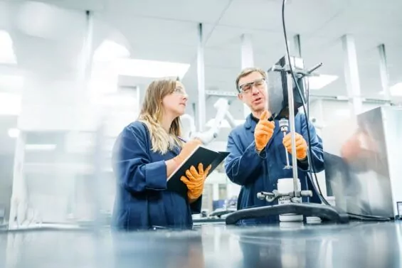 Man explains manufacturing tool to young female apprentice.