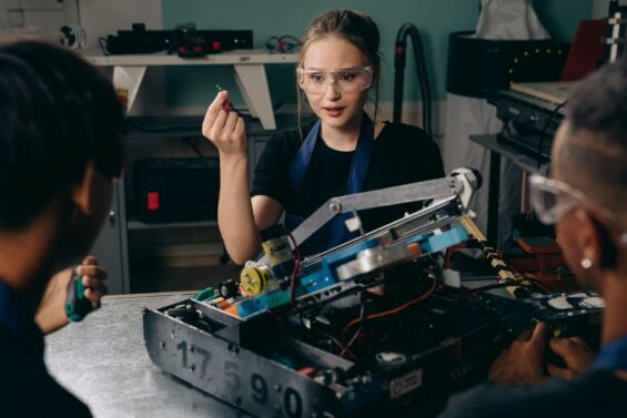 Young woman works on an engineered robot with colleagues.