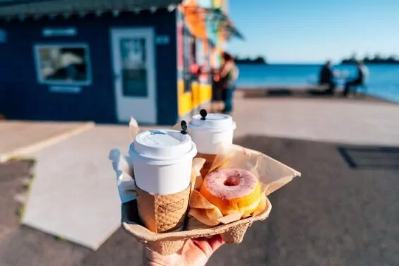Person holds two coffees and a donut from Jamesen's Fish Market & Bakery.