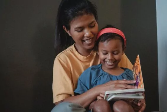 Mother reading to smiling daughter.