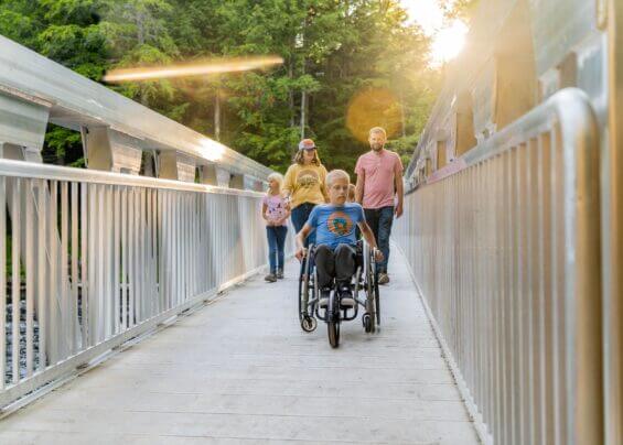 Family with a son in a wheel chair smiling and crossing a bridge.