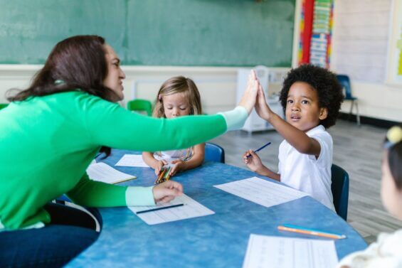 Teacher high fives young student at a table.