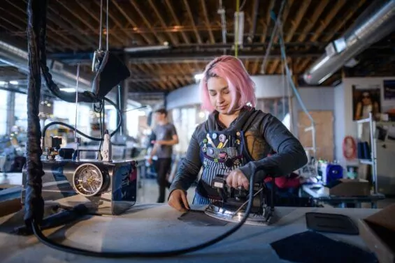 Young woman with pink hair irons jean pocket at Detroit Denim Company.