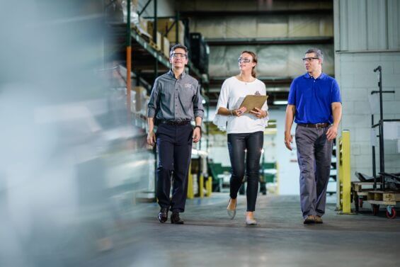 Three people in professional attire walk through factory.