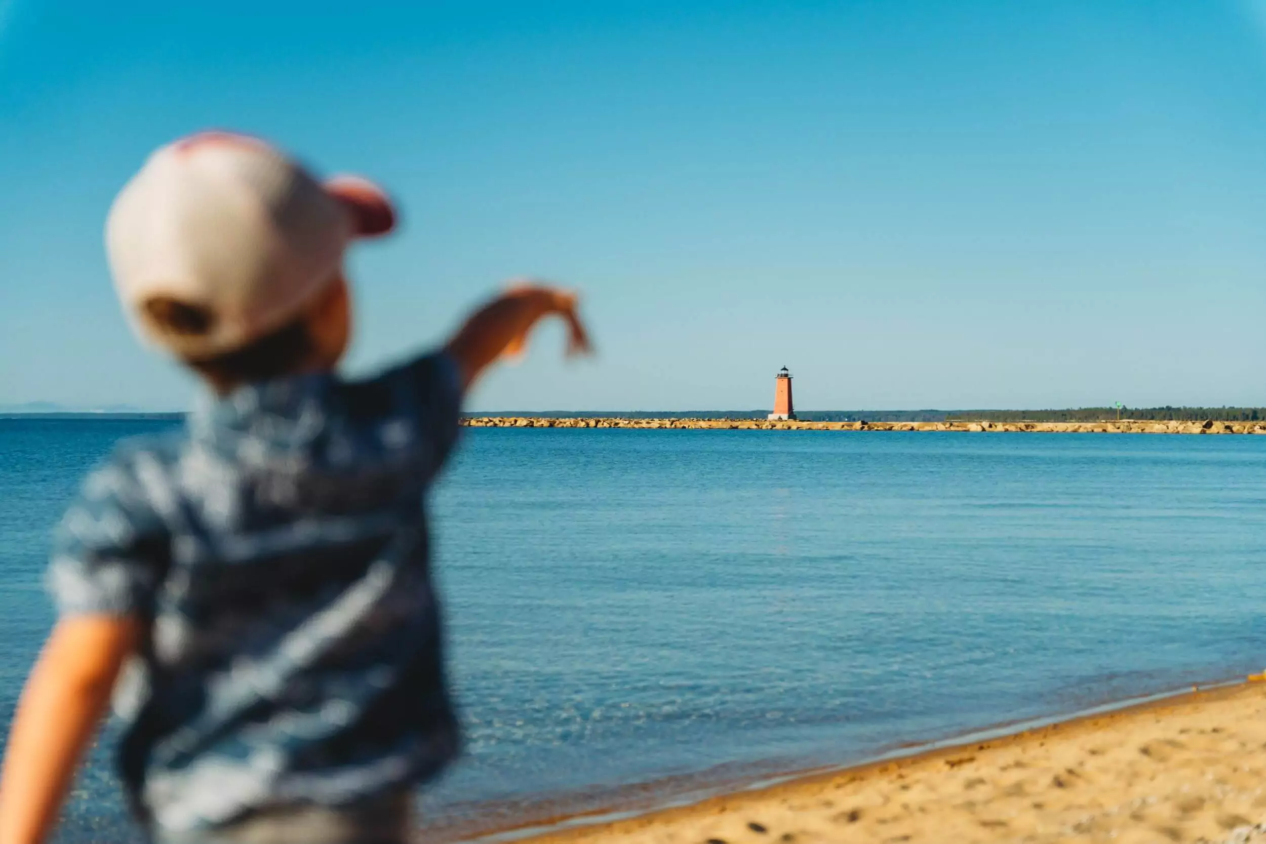 Small child points to lighthouse on beach in Manistique.