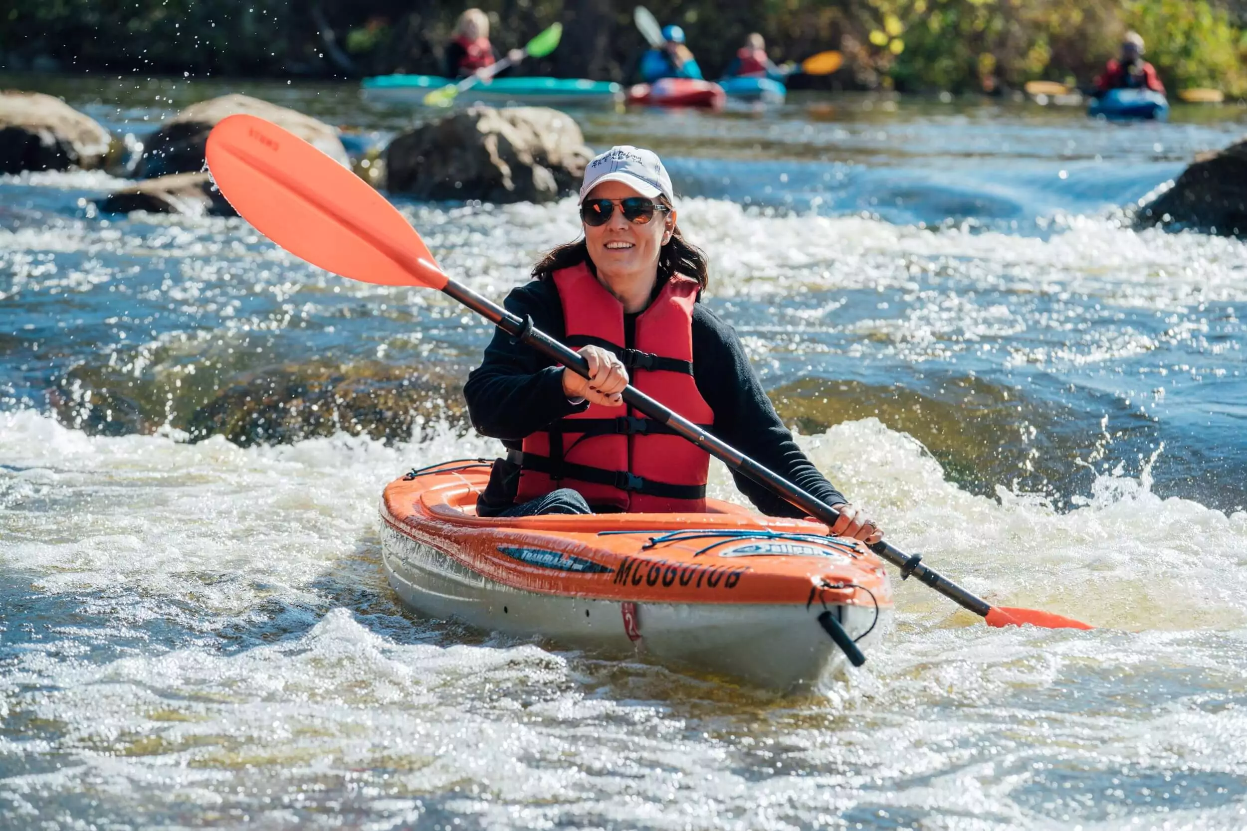 Women smiling and kayaking on rapids.
