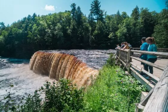 People look at Tahquamenon Falls, a waterfall in the Upper Peninsula, on a sunny day.