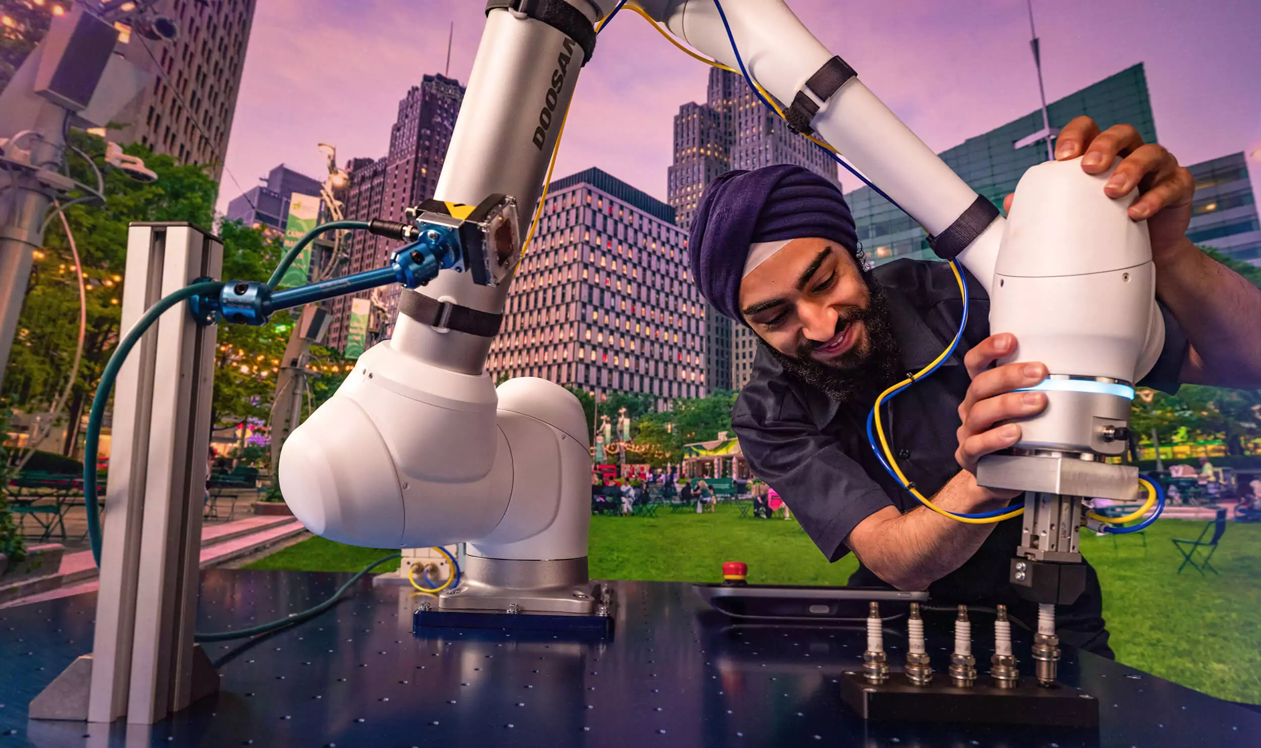 An engineer using a large, modern robotic arm to screw in a sizable bolt juxtaposed over a green, bustling park in downtown Detroit.